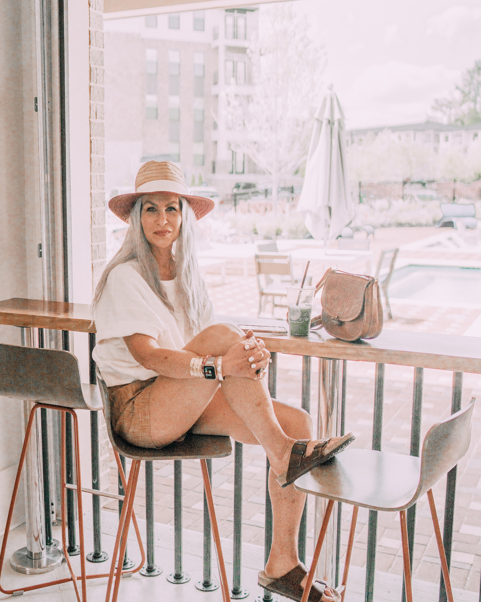Lisa wearing a straw brim hat and white shirt and linen shorts from Athleta. Also birkenstocks and a brown leather purse